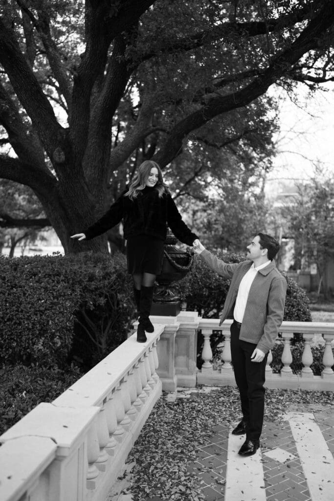 a man holding a girls hand as she walks on a railing during their engagement photoshoot