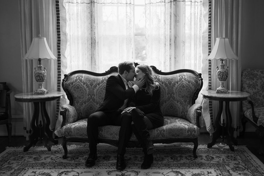 A man and a woman sitting on a vintage couch kissing during their engagement photos